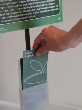 Future Fountain: Flyer wird aus dem Halter am Schild genommen